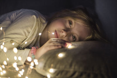 Portrait of girl lying on illuminated bed