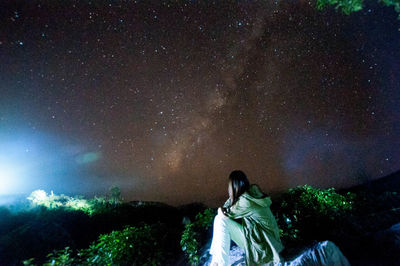 Rear view of woman sitting against star field at night