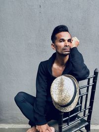 Portrait of young man sitting on chair against wall