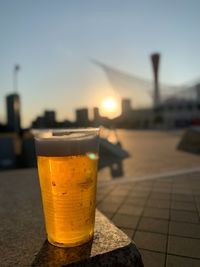 Close-up of beer glass on table against sky during sunset