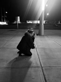 Rear view of woman sitting on floor in illuminated city at night