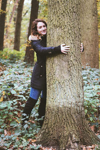 Portrait of young woman standing by tree trunk in forest