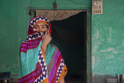 Portrait of indian woman standing against door covering face with her sari