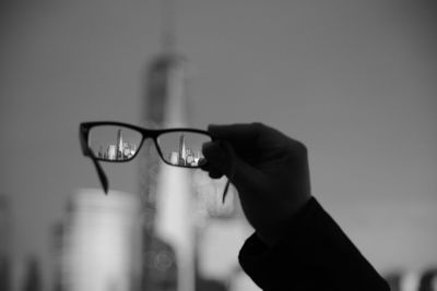 Cropped hand holding eyeglasses against buildings