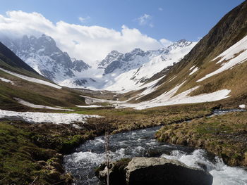 Scenic view of stream amidst snowcapped mountains against sky