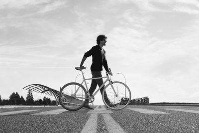 Side view of man with bicycle walking on road against sky