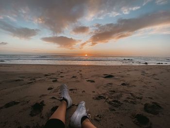 Low section of person on beach against sky during sunset