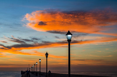 Street light by sea against sky during sunset