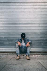 Full length of man sitting against wall