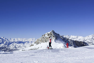 Low angle view of people skiing on snowy landscape against clear blue sky