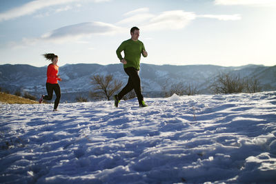 Couple jogging on snow field against sky