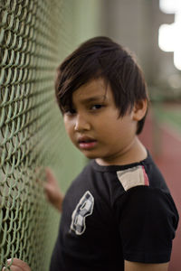 Close-up portrait of boy standing by chainlink fence