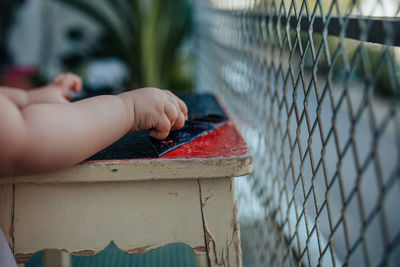 Cropped hands of baby removing plastic from stool by fence