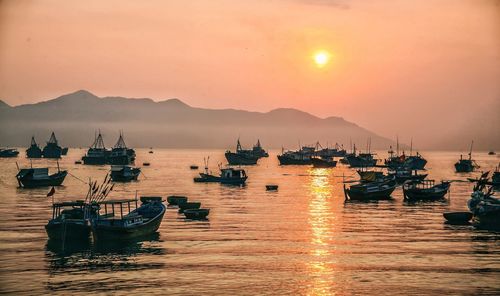 Boats moored at harbor against sky during sunset