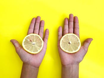 Close-up of hand holding fruit against yellow background