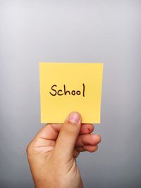 Cropped hand of person holding school text on adhesive note against gray background