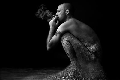 Side view of man with dirt smoking cigarette against black background