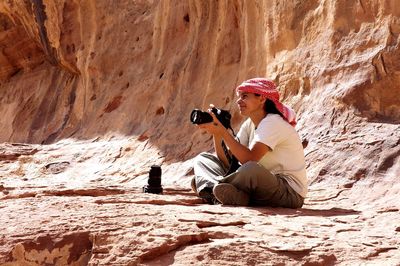 Young woman photographing while sitting on rock formation