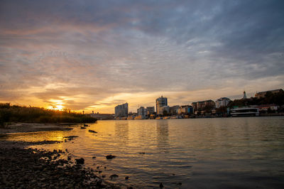 Scenic view of river by buildings against sky during sunset