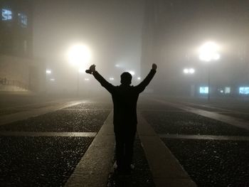 Silhouette man standing on illuminated lamp at night