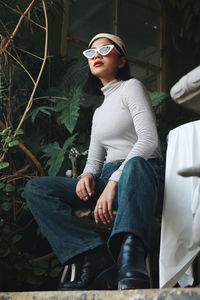 Low angle view of young woman wearing sunglasses sitting on chair