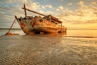 Abandoned ship fishing boat on beach against sky during sunset