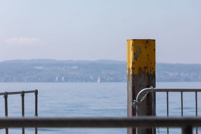 Close-up of metal railing by sea against sky
