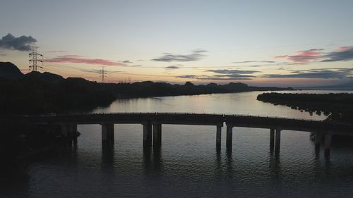 Silhouette bridge over lake against sky during sunset