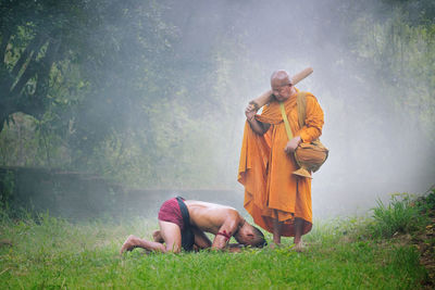 Mid adult man kneeling in front of monk on grassy field