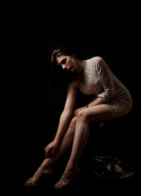 Young woman sitting against black background