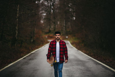 Portrait of young man standing on road in forest