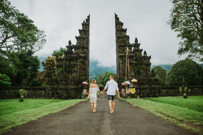 Couple walking on footpath at gate against sky