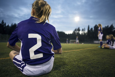 Rear view of girl sitting on field against sky