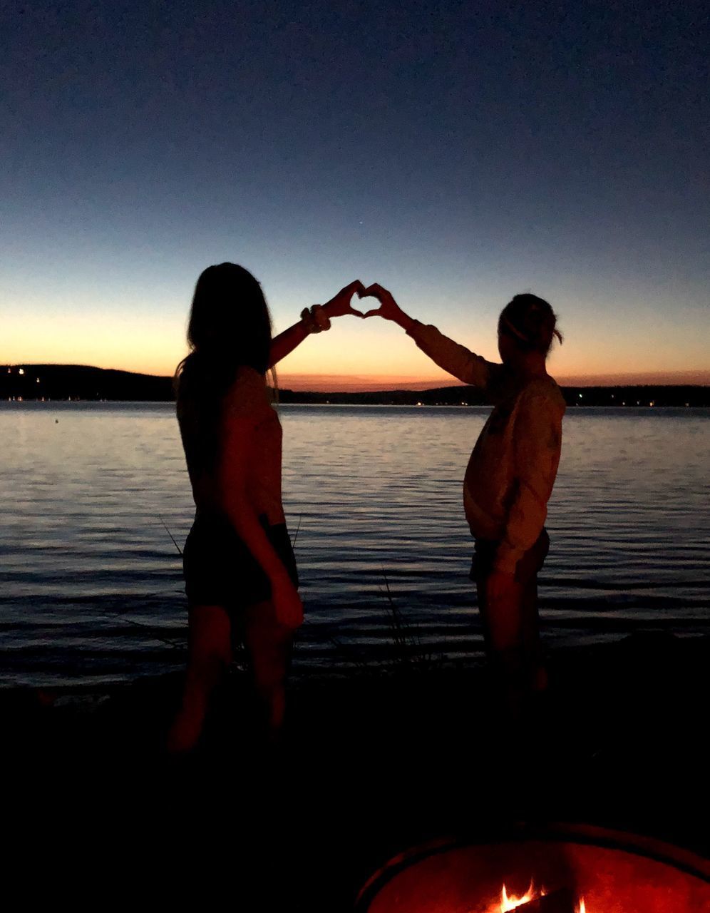 REAR VIEW OF FRIENDS STANDING ON LAKE AGAINST SKY DURING SUNSET