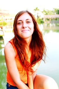 Portrait of smiling woman sitting against lake