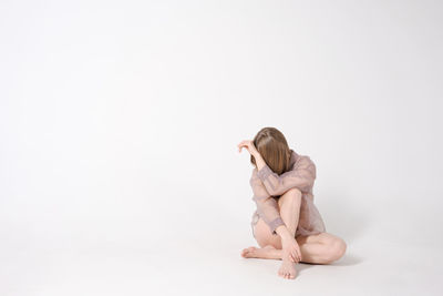 Woman is sitting on light background in studio. she is sad and depressed