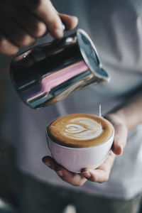 Midsection of person pouring milk in cappuccino