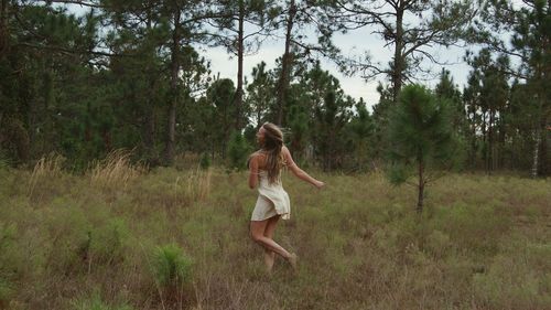 Cheerful woman dancing on grassy field against trees in forest