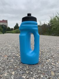 Close-up of blue bottle on road in city against sky