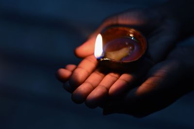 Close-up of cropped hand holding lit diya at night