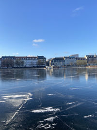 Scenic view of frozen river against blue sky in city