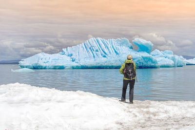 Rear view of woman standing at lake against sky during winter