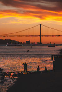 Silhouette bridge over sea against orange sky