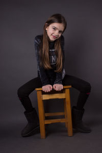 Young woman sitting on chair against gray background