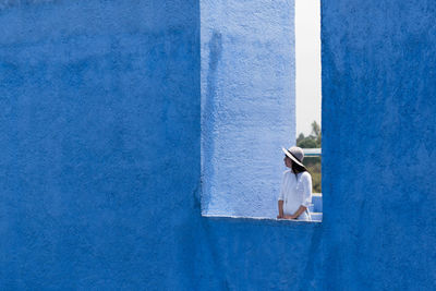 Young woman standing by blue wall