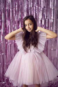 Beautiful girl with big eyes in a pink dress stands against the background of new year's tinsel