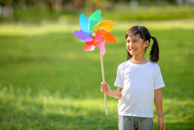 Cute little girl asia playing on the colorful toy windmill in her hands at the lawn.