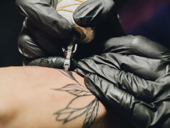 Cropped image of female artist making tattoo on male customer hand