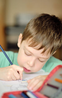 Cute and smiling cucasian boy draws with colored pencils while sitting at the table