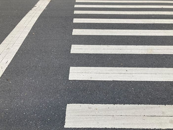 White crosswalk sign on grey asphalt road with a white straight line on the left side of it